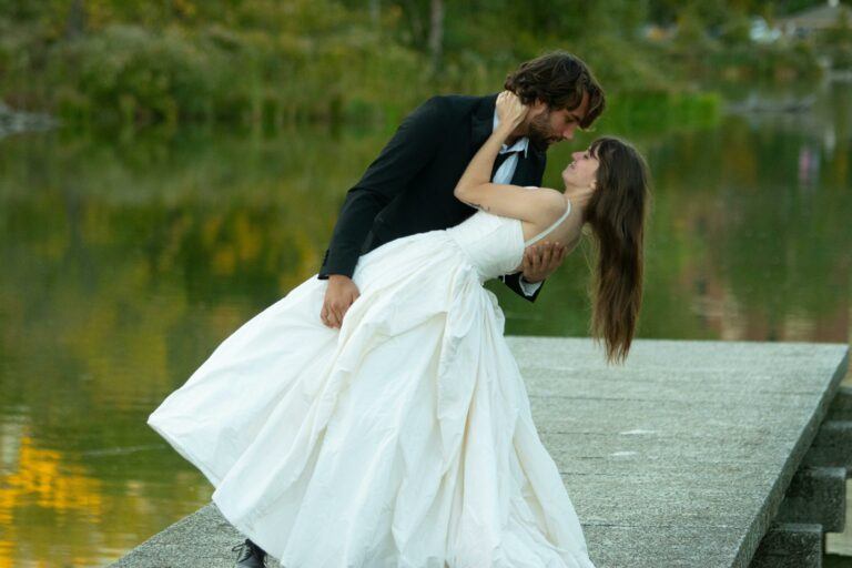 Couple in wedding attire dancing by a serene lake. Romantic and natural setting.